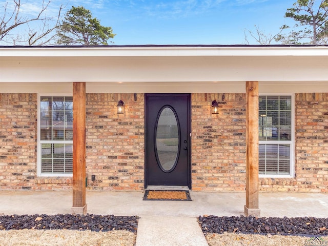 doorway to property with covered porch and brick siding