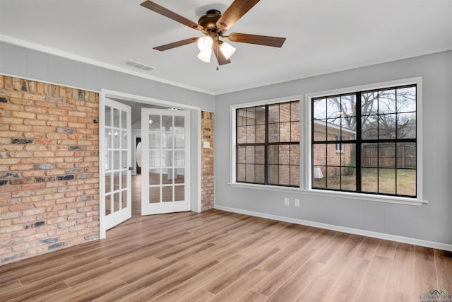 empty room with a wealth of natural light, brick wall, visible vents, and wood finished floors