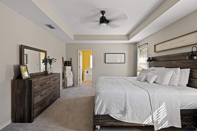 bedroom with ceiling fan, a raised ceiling, light colored carpet, and ensuite bath