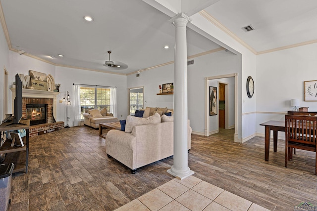 living room with ornate columns, ceiling fan, a brick fireplace, crown molding, and hardwood / wood-style flooring