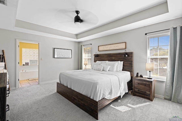 bedroom featuring a tray ceiling, ensuite bath, ceiling fan, and multiple windows