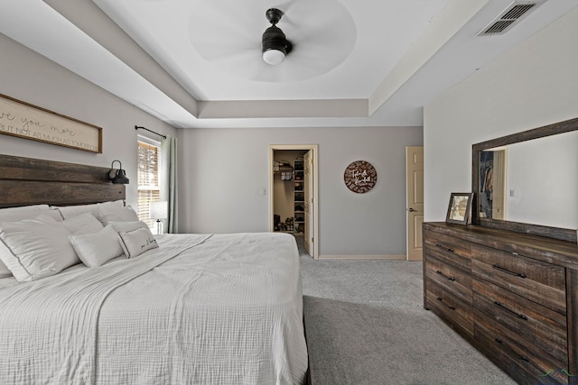 carpeted bedroom featuring ceiling fan, a closet, a spacious closet, and a tray ceiling