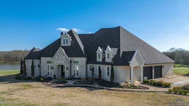 french country inspired facade featuring a garage, a water view, and a front lawn