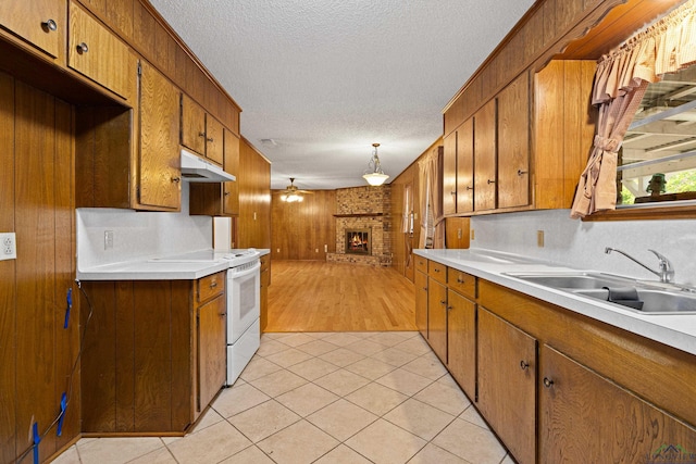 kitchen featuring under cabinet range hood, a sink, brown cabinets, and electric range