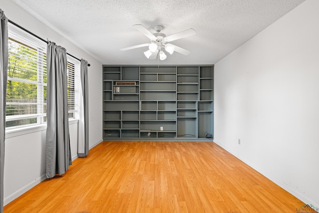 empty room featuring ceiling fan, baseboards, a textured ceiling, and light wood-type flooring