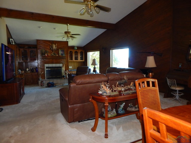 carpeted living room featuring vaulted ceiling with beams, a large fireplace, ceiling fan, and wooden walls