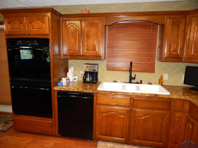 kitchen with light stone countertops, decorative backsplash, sink, and black appliances