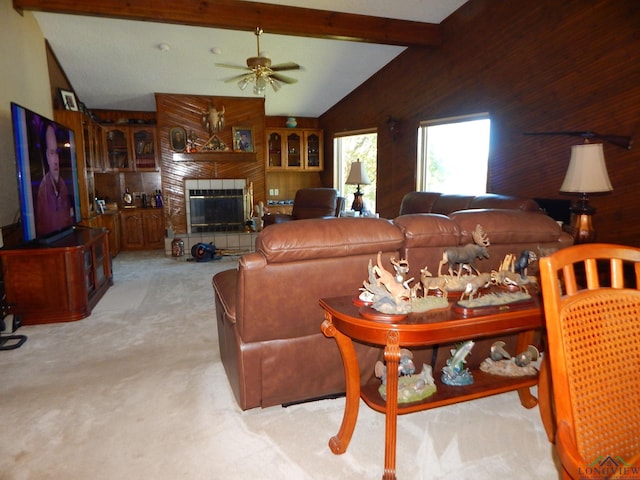 carpeted living room featuring vaulted ceiling with beams, ceiling fan, wooden walls, and a tiled fireplace