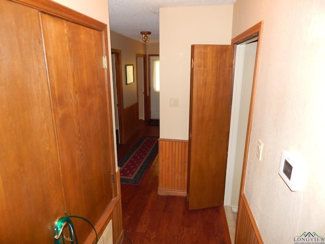 hall with a textured ceiling, dark wood-type flooring, and wooden walls