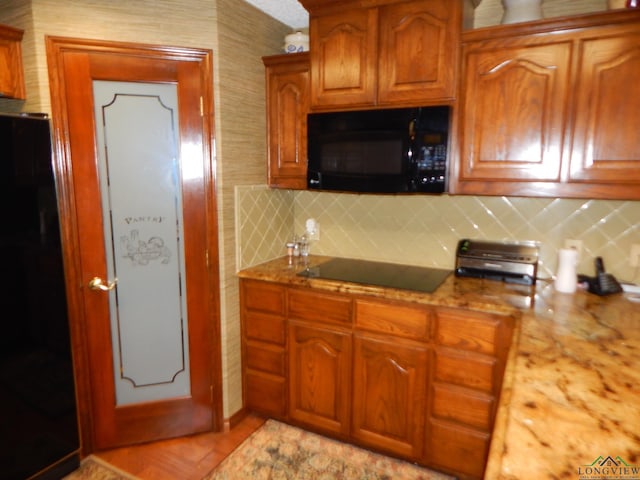 kitchen featuring backsplash, light stone counters, and black appliances