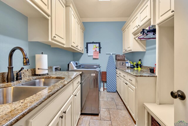 kitchen featuring light stone counters, washing machine and clothes dryer, stone tile flooring, a sink, and baseboards