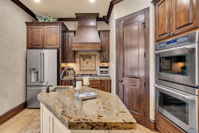 kitchen with custom range hood, stainless steel appliances, ornamental molding, and an island with sink