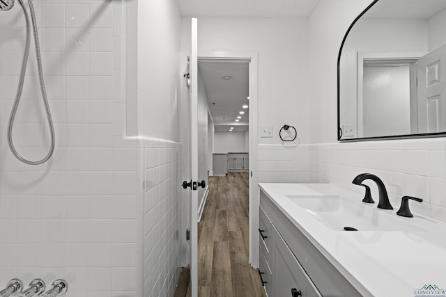 bathroom featuring hardwood / wood-style floors, vanity, tiled shower, and tile walls