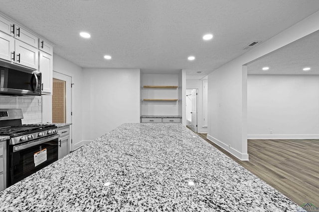 kitchen with tasteful backsplash, white cabinetry, light stone countertops, and stainless steel appliances