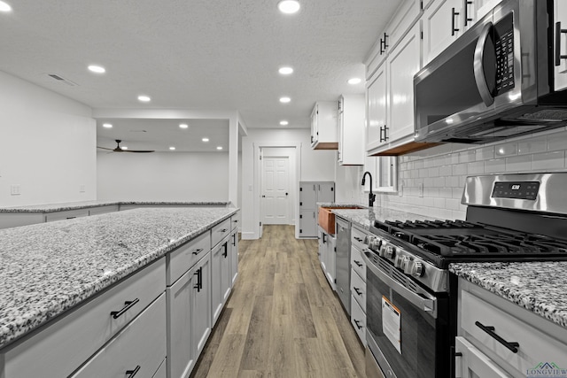 kitchen featuring white cabinets, ceiling fan, light stone countertops, light hardwood / wood-style floors, and stainless steel appliances