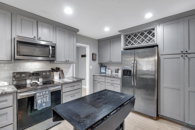 kitchen with gray cabinetry, appliances with stainless steel finishes, light wood-type flooring, light stone countertops, and tasteful backsplash