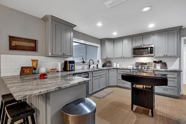 kitchen with stainless steel appliances, a sink, a peninsula, and gray cabinetry