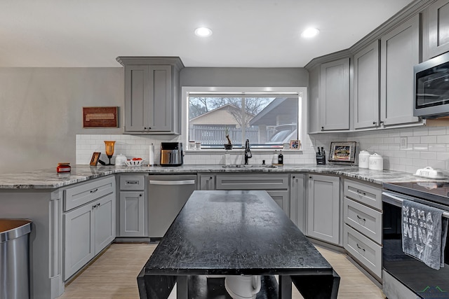 kitchen featuring light wood finished floors, appliances with stainless steel finishes, light stone counters, gray cabinetry, and a sink