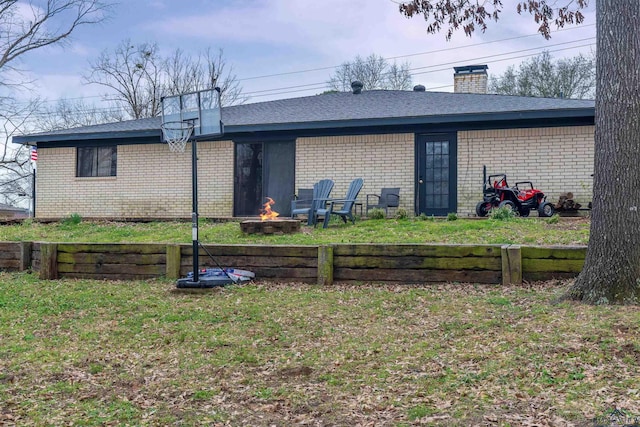 back of house featuring an outdoor fire pit, brick siding, a yard, and a chimney