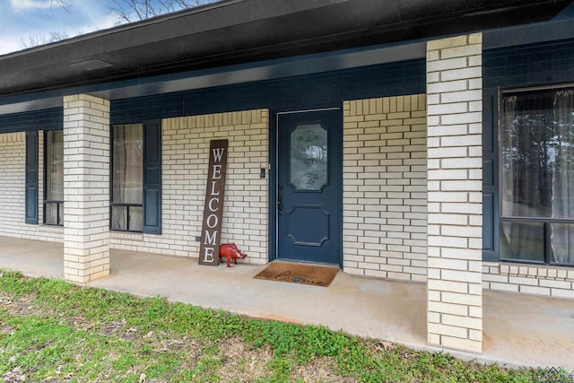 view of exterior entry featuring covered porch and brick siding