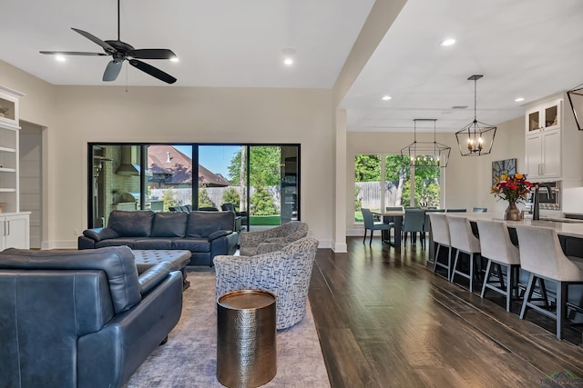 living area with ceiling fan with notable chandelier, baseboards, dark wood-type flooring, and recessed lighting