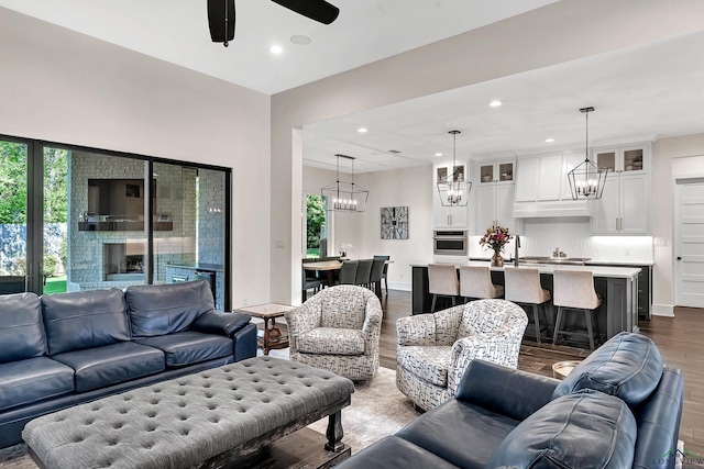 living room with ceiling fan with notable chandelier, baseboards, dark wood-style floors, and recessed lighting