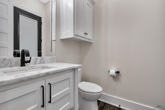 bathroom featuring toilet, vanity, wood finished floors, and baseboards