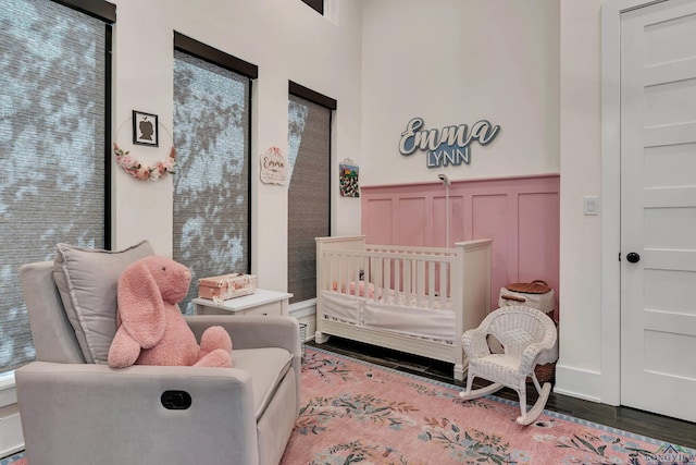 bedroom with wainscoting, a nursery area, a decorative wall, and wood finished floors