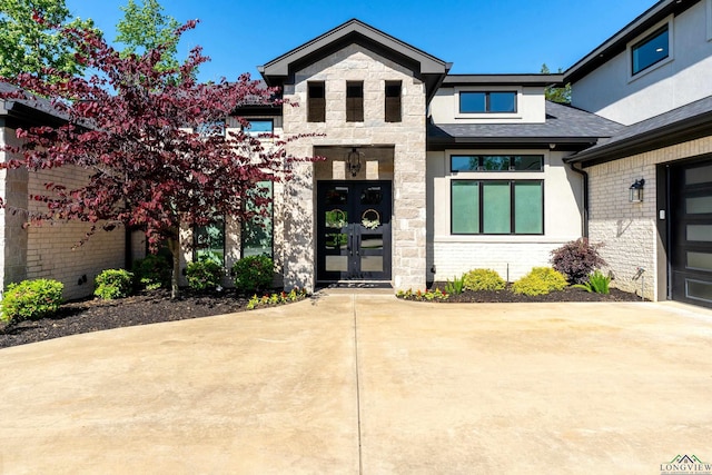 view of exterior entry with stone siding, a shingled roof, and french doors