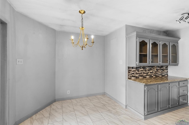 unfurnished dining area featuring a notable chandelier, marble finish floor, and baseboards