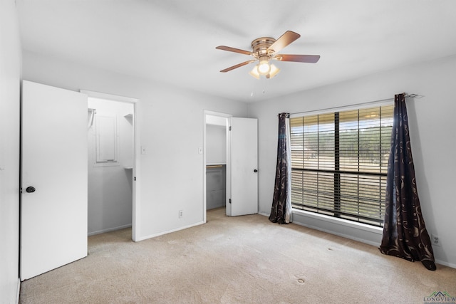 unfurnished bedroom with a walk in closet, a ceiling fan, baseboards, and carpet floors