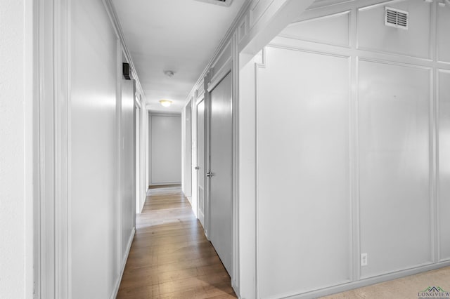 hall featuring light wood-type flooring, visible vents, and a decorative wall