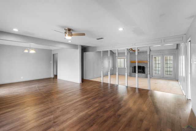 unfurnished living room featuring visible vents, a brick fireplace, recessed lighting, ceiling fan with notable chandelier, and wood finished floors