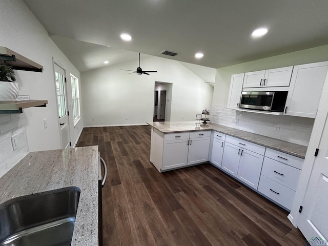 115 Alta St, Longview, TX 75604 - kitchen featuring stainless steel microwave, a peninsula, light stone countertops, decorative backsplash, and white cabinetry