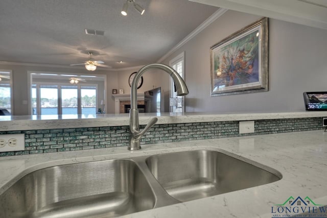 room details with sink, a textured ceiling, ornamental molding, ceiling fan, and light stone countertops