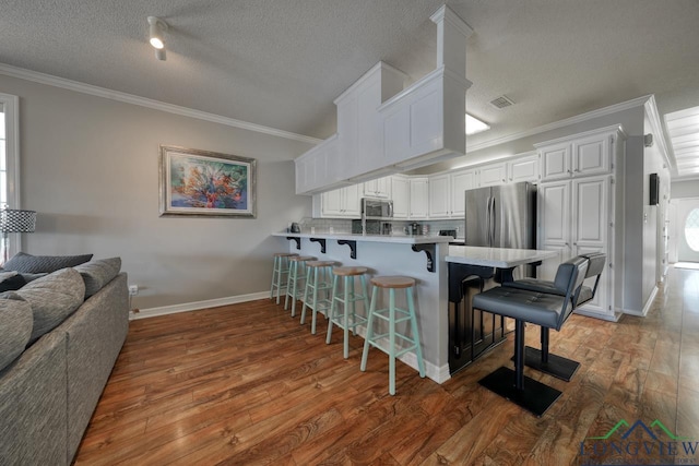 kitchen featuring appliances with stainless steel finishes, backsplash, white cabinets, a kitchen breakfast bar, and kitchen peninsula