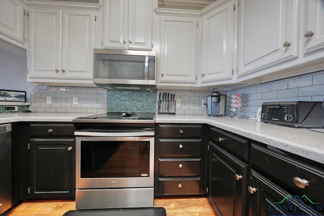 kitchen featuring appliances with stainless steel finishes, tasteful backsplash, white cabinetry, light stone counters, and light hardwood / wood-style flooring