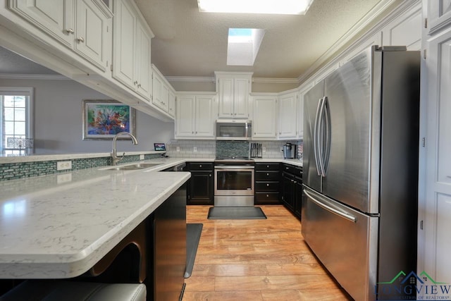 kitchen with appliances with stainless steel finishes, sink, white cabinets, a kitchen bar, and kitchen peninsula