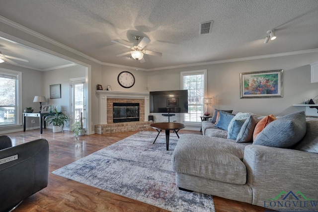 living room with rail lighting, ceiling fan, crown molding, a brick fireplace, and a textured ceiling