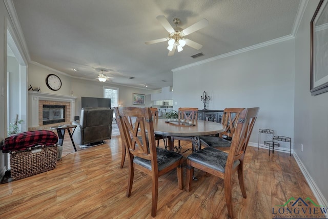 dining area with crown molding, ceiling fan, light hardwood / wood-style floors, and a brick fireplace