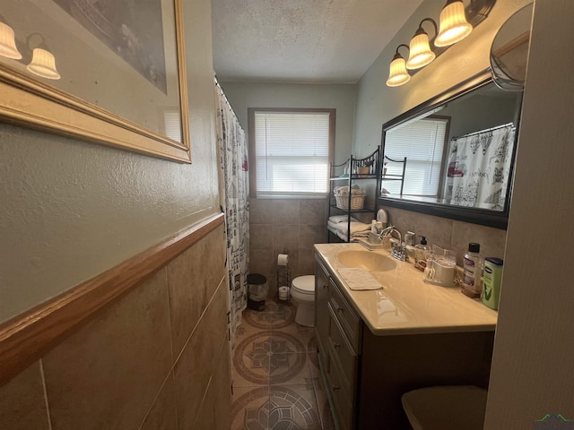 bathroom with tile walls, tile patterned flooring, vanity, a textured ceiling, and toilet