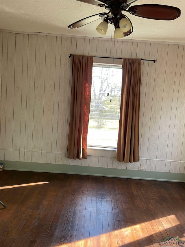 unfurnished room featuring ceiling fan, wood walls, and dark wood-type flooring