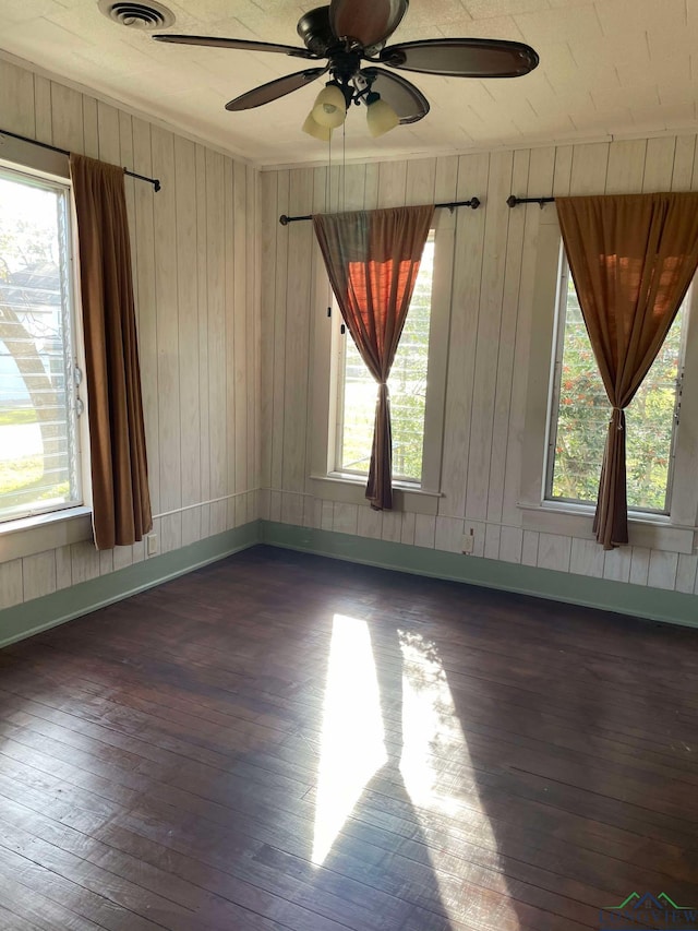 empty room with ceiling fan, a healthy amount of sunlight, dark hardwood / wood-style flooring, and wooden walls