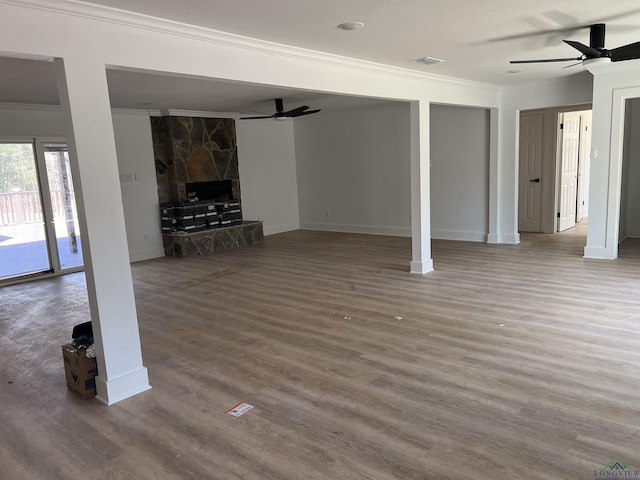 unfurnished living room featuring wood-type flooring, a stone fireplace, ceiling fan, and crown molding