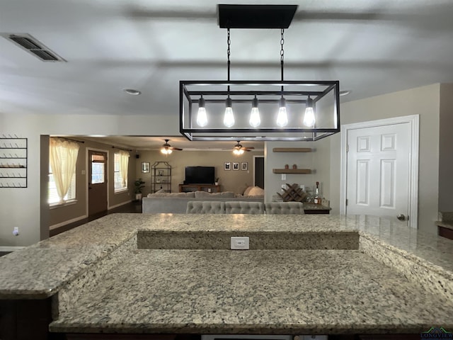 kitchen with ceiling fan, a kitchen island, and light stone counters