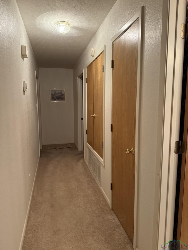 corridor with a textured ceiling and light carpet