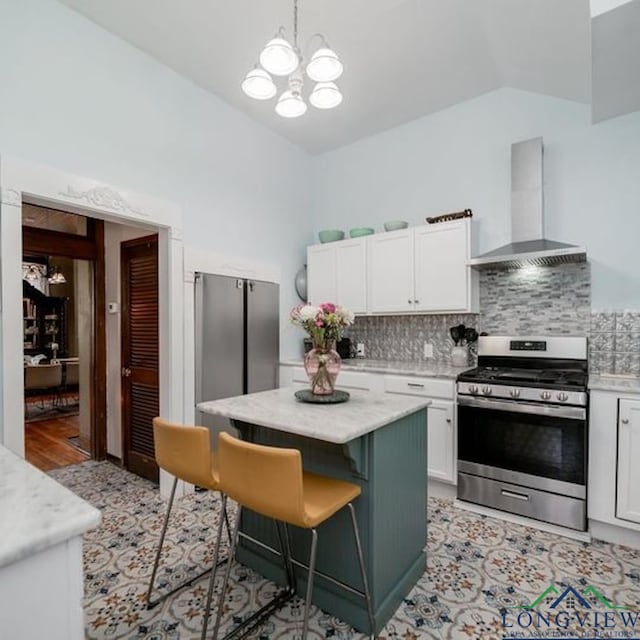 kitchen featuring a breakfast bar, stainless steel range with gas stovetop, a kitchen island, wall chimney range hood, and white cabinets