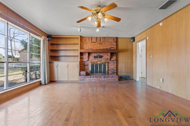 unfurnished living room featuring ceiling fan, built in features, a fireplace, a textured ceiling, and wooden walls