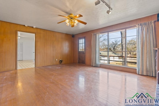 unfurnished room with wooden walls, plenty of natural light, and a textured ceiling