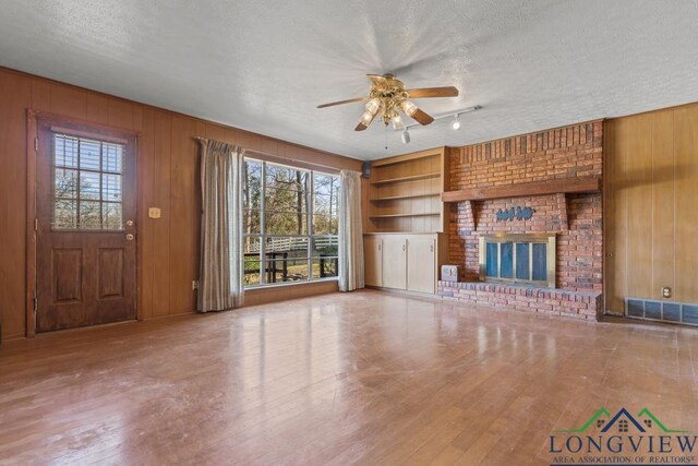 unfurnished living room featuring wooden walls, built in features, plenty of natural light, and a textured ceiling